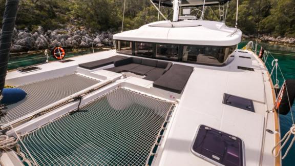 The Daphne catamaran anchored in clear waters, featuring nets and a comfortable lounging area on the foredeck.