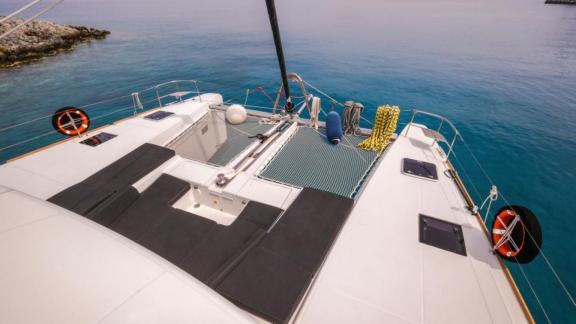 The foredeck of the Daphne catamaran features sun loungers and nets, anchored in calm, clear waters.