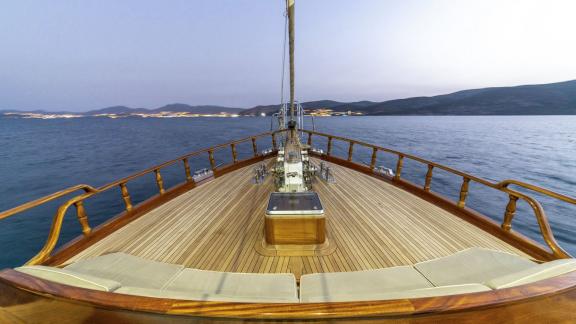 Deck einer luxuriösen Holz-Segelyacht bei Dämmerung mit Blick auf das Meer und die Küste von Bodrum.