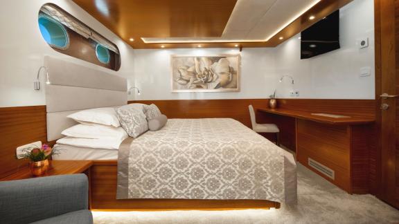 Стильная каюта на яхте Son de Mar с уютной кроватью, рабочим столом и элегантным освещением.