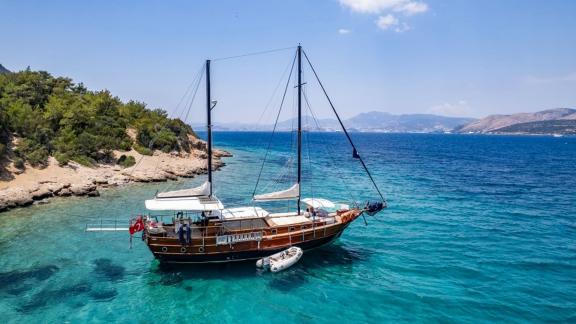 The elegant Gulet Golden Joy anchored in a turquoise bay, surrounded by picturesque scenery.