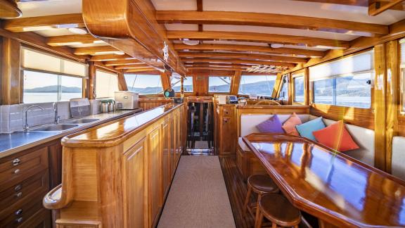 The interior features a kitchen, a dining table with colorful cushions, and a helm station.