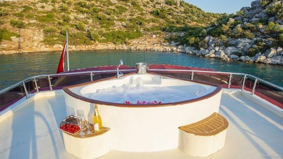 Jacuzzi on the deck of the gulet Vesta 1 Sevil, with champagne and fruit, in front of a picturesque coastline.