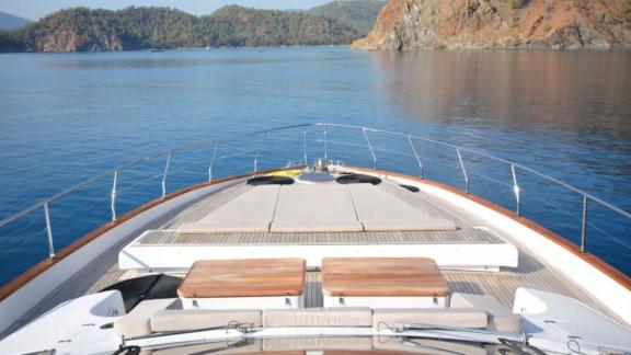 Spacious foredeck of a luxurious motor yacht with an idyllic coastal view.