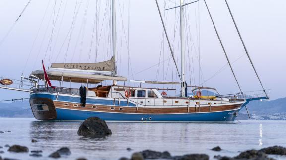 Elegant gulet Gozdem The One anchored in the waters of Bodrum, blue hull, wooden panelling, picturesque background.