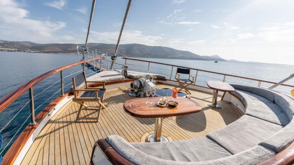 Sun deck of the gulet Gozdem The One with comfortable seating and table, surrounded by clear waters and hills in Bodrum.