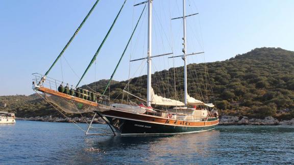 A luxurious gulet yacht named Grande Mare is anchored in clear, calm waters surrounded by wooded hills.