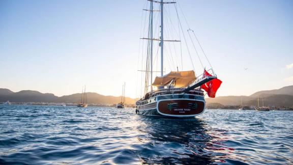 A magnificent red-flagged sailing yacht anchored in calm waters at sunset