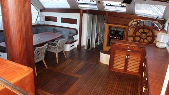 Interior of the Grande Mare with cosy seating area, dining table and steering wheel. Ideal for comfortable yacht charter