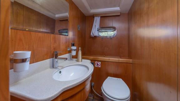 A modern bathroom on a Bodrum gulet with wood panelling, washbasin, mirror and toilet.