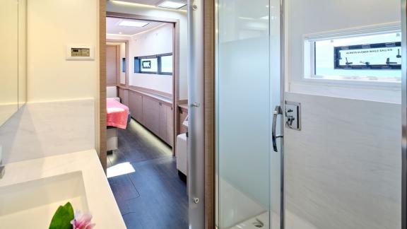 Modern bathroom on the catamaran with a shower, sink, and view into the adjacent cabin.