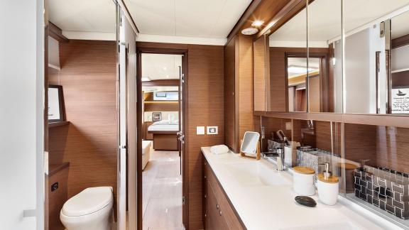 Modern bathroom with sink, large mirrors, and access to a cabin with a double bed in Emerald Gemini catamaran.