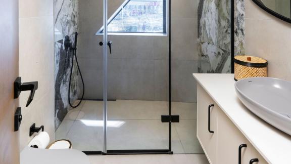 Stylish and modern bathroom with glass shower cabin, large sink, and mirrors with black frames.