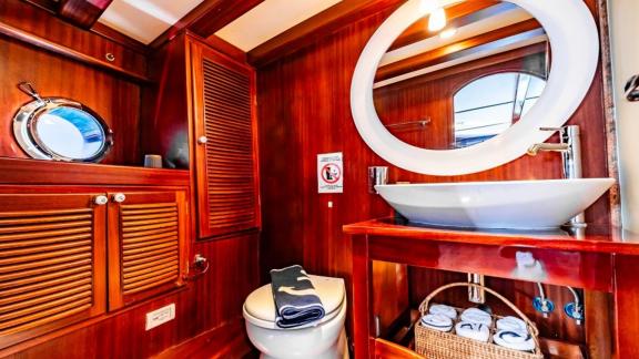 Elegant bathroom with round mirror, sink, and wooden cabinets on Gulet Golden Joy in Bodrum.