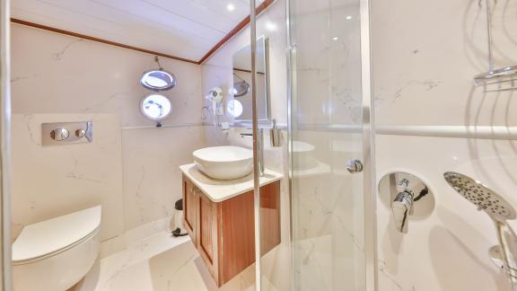 A modern bathroom on the Gulet Kasapoglu 6 featuring a shower, sink, and marble paneling.