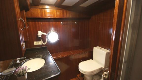 Stylishly furnished bathroom on the Diamond Lila with fine wooden furniture, marble washbasin and sea view through the p