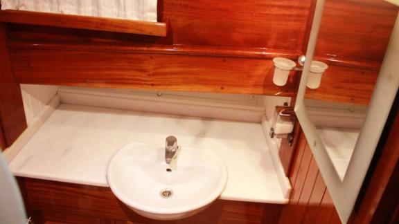 A bathroom on Gulet Il Fratello with a white sink, a mirror, and wood paneling.