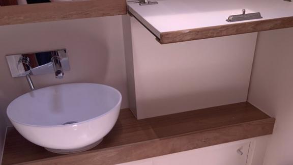 The bathroom of the Deneb sailing yacht features a round sink on a wooden counter.