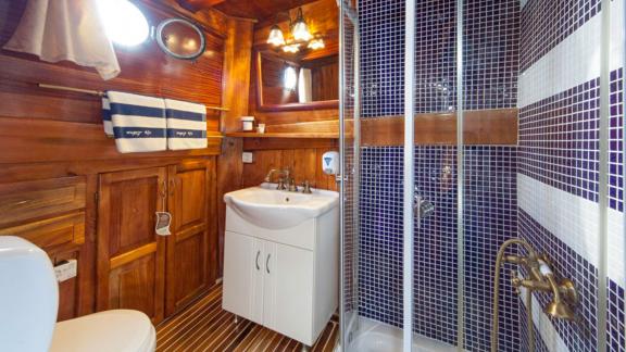 Bathroom on a gulet with wooden interior, blue tiles, shower and washbasin.