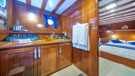 High-quality bathroom with wooden walls, modern washbasin and towels, adjoining a cosy bedroom.