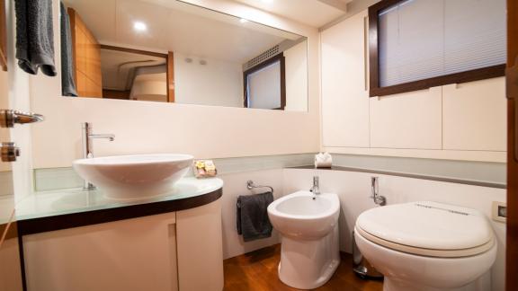Das Badezimmer bietet Waschbecken, Toilette und Bidet. Großes Spiegelpaneel und Holzfußboden sorgen für Helligkeit.