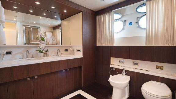 The bathroom features dark wood cabinets, a wide mirror, double sinks and round porthole windows.