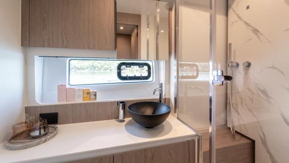 A stylish bathroom featuring a glass shower cabin, marble-patterned wall, and modern black sink.