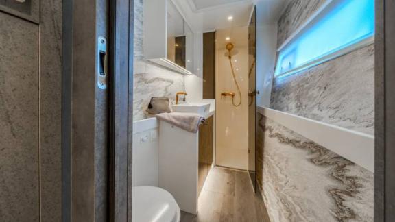 Ванная с мраморными стенами, окном, золотым душем и краном, зеркальным шкафом и туалетом.