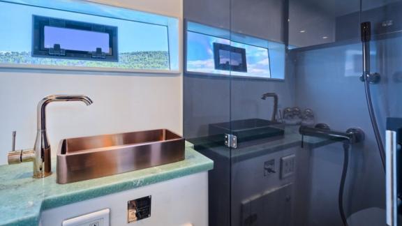 Ванная комната оснащена стеклянной душевой кабиной, стильной раковиной и окном с видом на море.