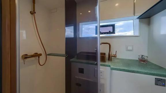 Luna 49 Blue banyosu altın duş takımı, geniş pencere ve yeşil tezgahlı lavabo alanıyla modern bir kullanım sunar.