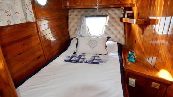 Single cabin with wooden walls, decorative pillows, and a porthole on Gulet Ali Aga 1 in Göcek.