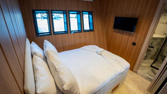 The luxurious bedroom of Almila motor yacht in Marmaris features a comfortable bed, TV, and windows.