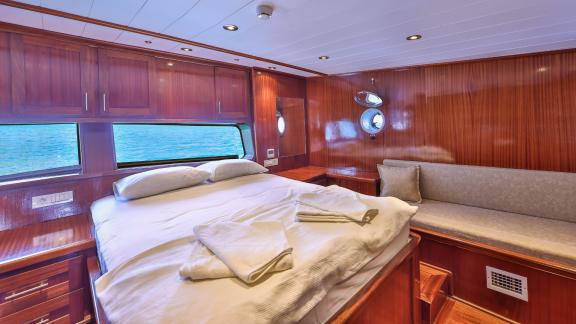 A comfortable cabin on the Gulet Kasapoglu 6 featuring a double bed, sofa, and sea view through large windows.