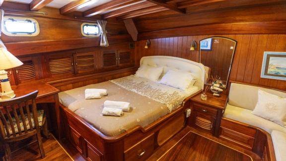 Cozy cabin of the Serenad yacht with a double bed, desk, and elegant wood furnishings.