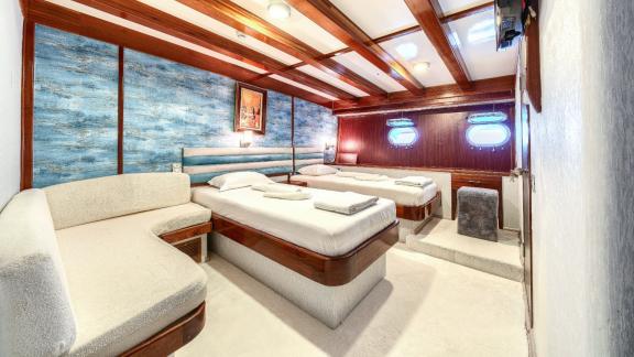 Bright cabin with three beds, wooden elements, blue wall decorations and porthole windows for a sea view.