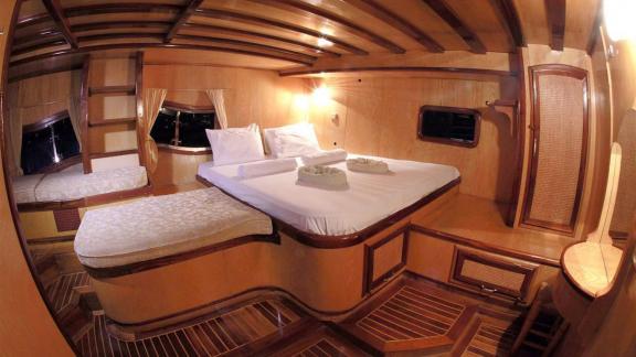 Cabin of Gulet Nirvana 2 with double bed, single bed, wooden walls, windows with curtains, and desk.