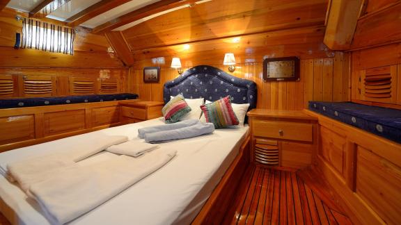 Cozy bedroom of Gulet Xenos 2 in Bodrum with warm wood paneling and a comfortable double bed.