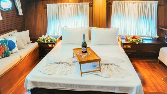 A cosy bedroom on a sailing ship, with an elegantly prepared bed and a bottle of champagne.