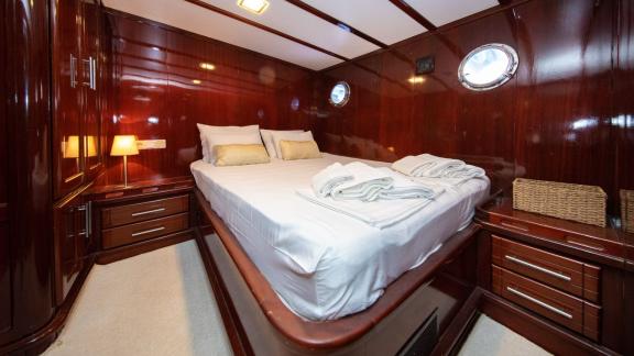 Cosy cabin on the Gulet Vivere with a large bed, elegant wooden furnishings and small portholes for natural light.