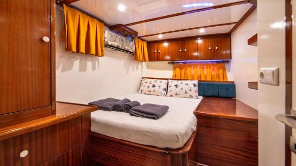 Guest cabin of Gulet Lycian Sirius featuring a double bed, wooden furniture, and orange curtains.