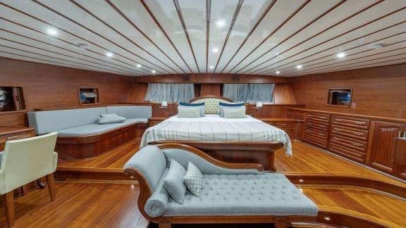 Bedroom on a boat with double bed, sofa, armchair and wooden interior.