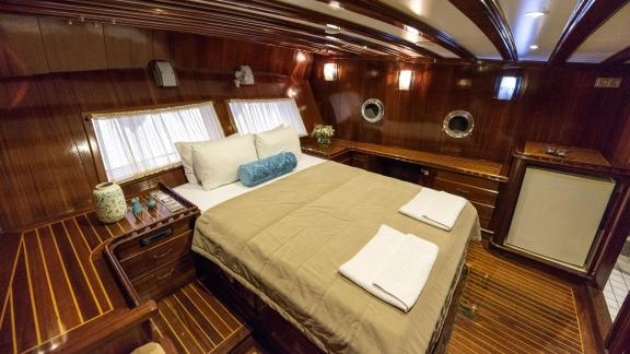 Comfortable bedroom on Gulet Ceylan with double bed, wooden furniture, and porthole windows.