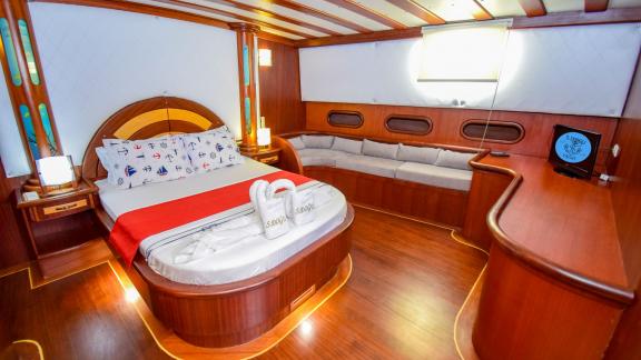 Geräumige Kabine auf einer Segelyacht mit einem großen Bett, einer Sitzecke und eleganten Holzmöbeln.