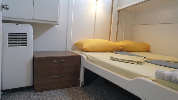 Cozy cabin with double bed, yellow linens, air conditioning, and a bedside table.