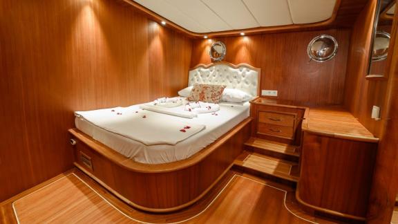 An elegant and comfortable sleeping cabin on the Gulet Anıl Kaptan 1 with wood paneling and a luxurious bed.