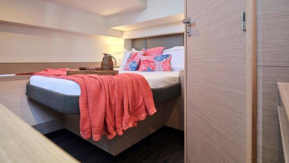 Cozy cabin on the catamaran with a double bed, soft coral blanket, and decorative pillows.