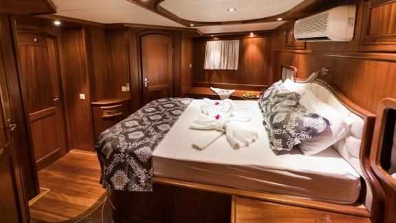 The master cabin of gulet Seven 1 features a cozy bedroom decorated with wooden accents.