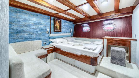 Cosy cabin with double bed, blue wall decoration, wooden elements and porthole windows for a sea view.