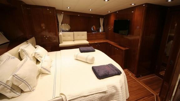 Luxurious cabin on the Gulet Didi with large bed, wood panelling, seating area and TV.