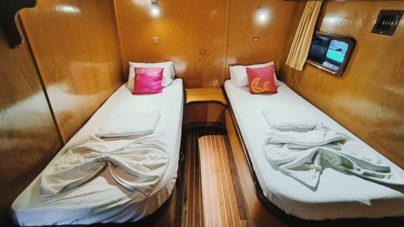 Cabin with two single beds, wooden walls, reading lamps, and windows with curtains on Gulet Nirvana 2.